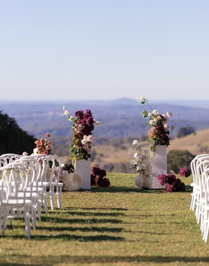 Outdoor wedding ceremony aisle styled with white chairs and floral plinths overlooking the Sunshine Coast hinterland